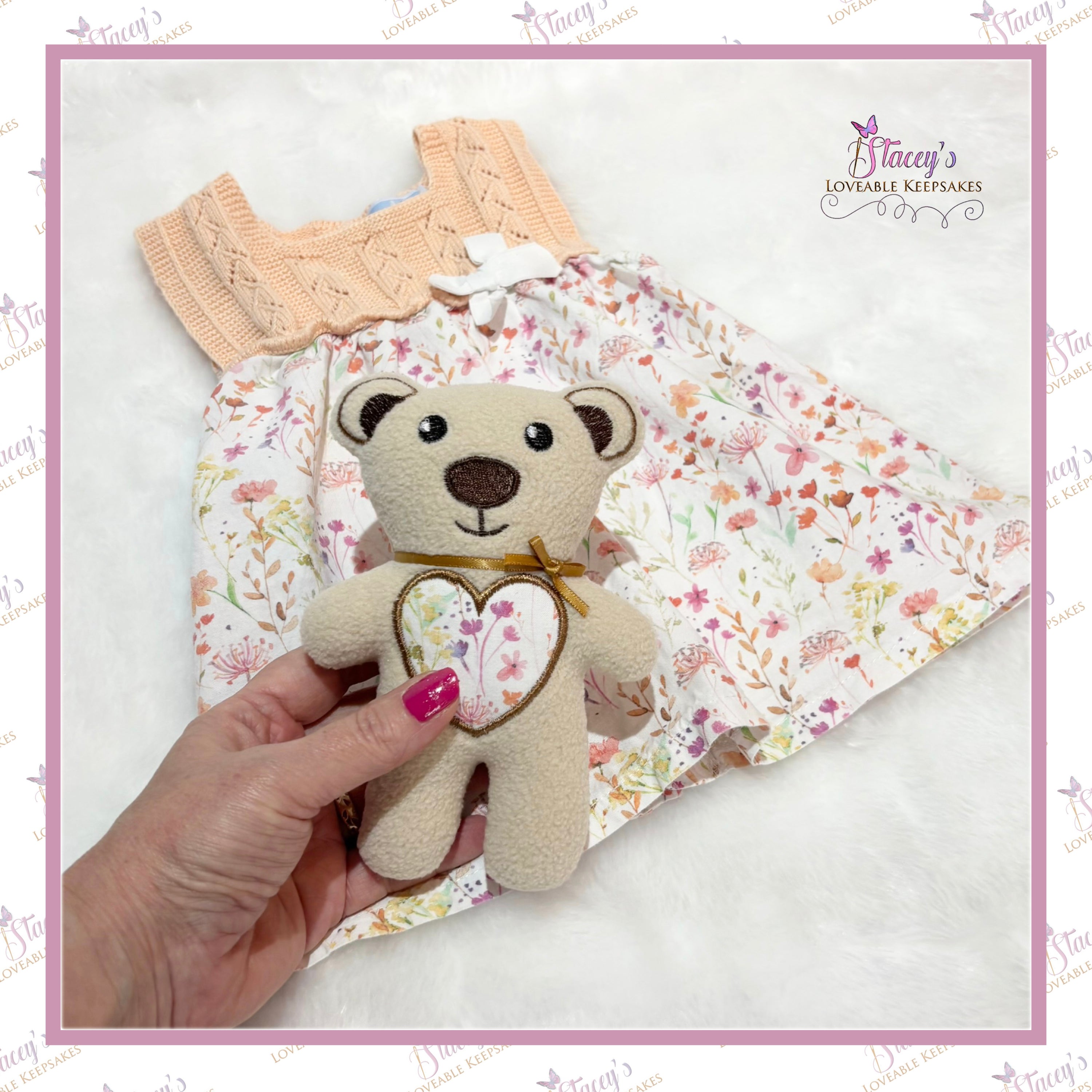 Hand holding a small teddy bear with a floral heart design, against a floral fabric background.