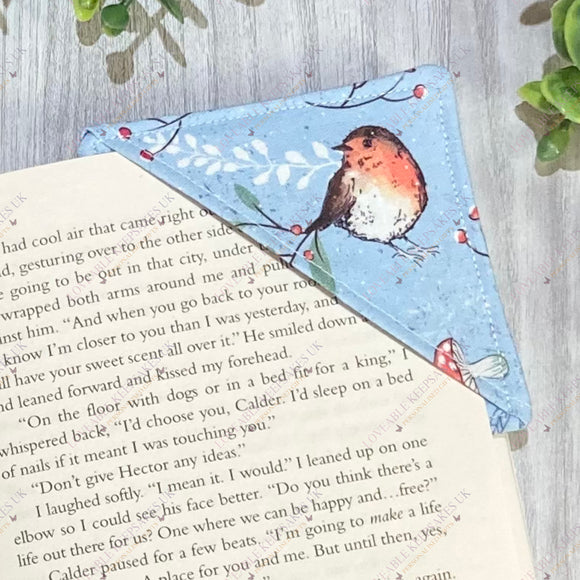 Handmade Christmas robin fabric corner bookmark shown on an open book page.
