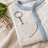 Memory heart keyring made from a baby’s first outfit, displayed on the matching multicoloured star-print sleepsuit beside a wooden rattle.