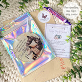 Complete packaging display showing the “Empty Chair” bauble in a holographic gift pouch, thank-you card, branded sticker and Parma Violets sweet.