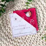 Red fabric bookmark with a bird design on a textured surface, accompanied by a card with branding.