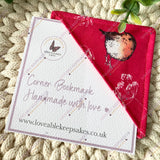 Corner bookmark with robin bird design on red fabric, placed on a textured surface.