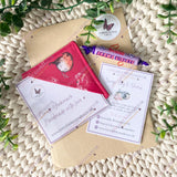 Packaging with a bookmark, card, and other items on a textured surface with greenery.