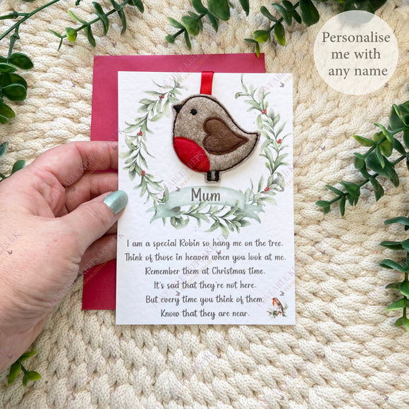 Person holding a personalised Christmas robin hanging decoration on a linen-textured poem card with “Mum” on the wreath banner.