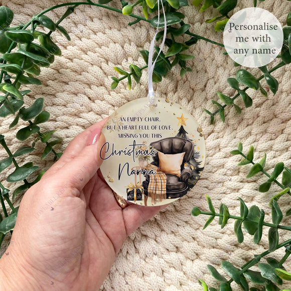 Empty Chair Christmas bauble personalised with the name Nanna, featuring an armchair, Christmas tree and robin design. Acrylic memorial bauble shown held in hand.