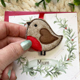 Hand holding a handmade felt robin hanging ornament with red ribbon, part of a Christmas remembrance keepsake.