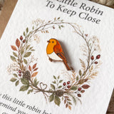 Close-up of the orange, brown and white robin enamel pin badge displayed inside an autumn woodland wreath with berries and pinecones.
