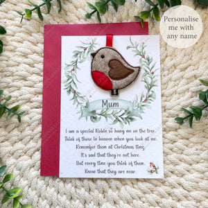 Person holding a personalised Christmas robin hanging decoration on a linen-textured poem card with “Mum” on the wreath banner.