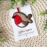 Single felt robin decoration laid flat on its remembrance card, showing embroidery details and red ribbon for hanging.
