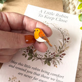 Removable orange, brown and white robin enamel pin badge held above its A6 remembrance poem card to show the detailed design.