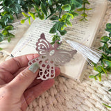 Hand holding silver plated stainless steel guardian angel bookmark to show size and detailed angel design with white tassel.
