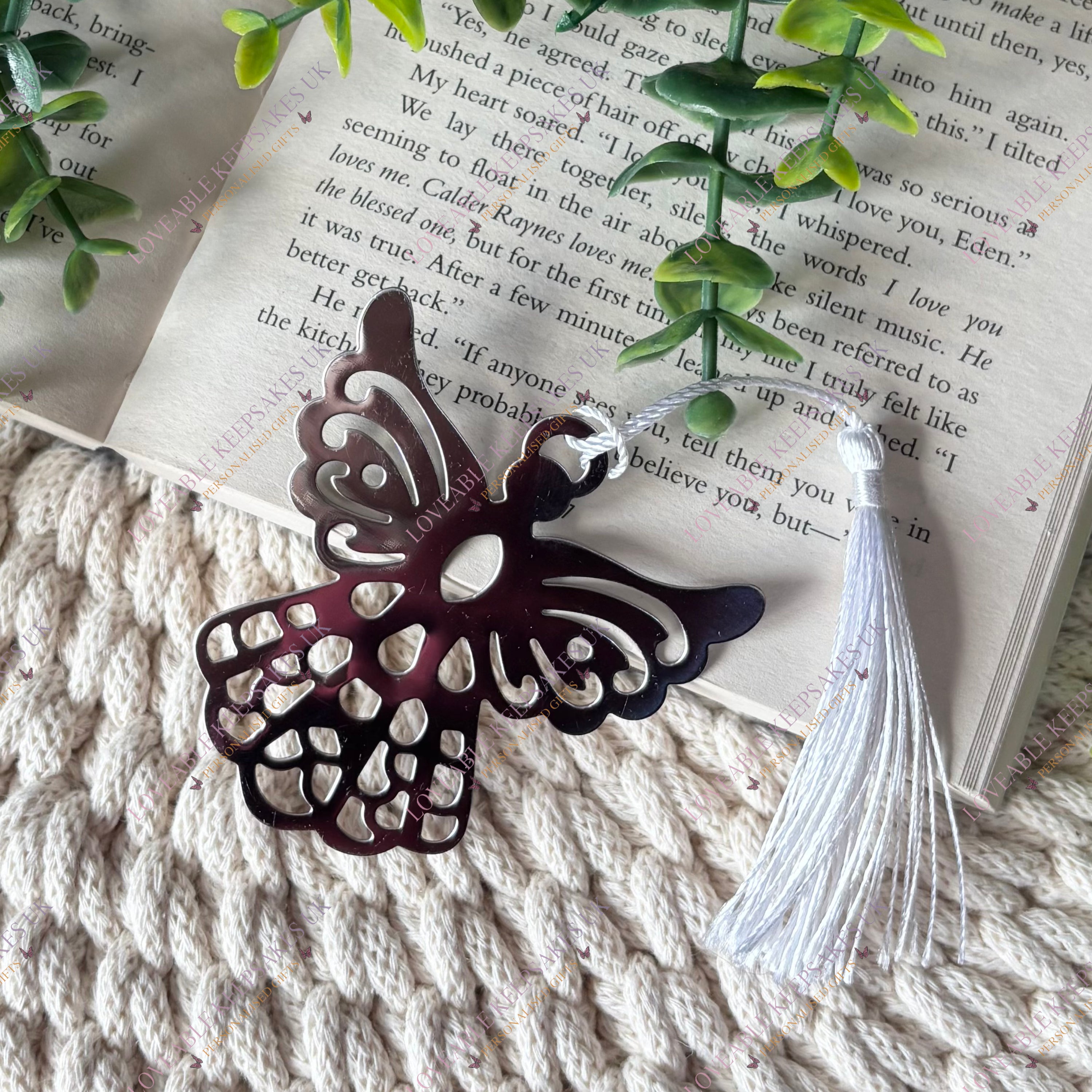 Silver guardian angel bookmark resting across the pages of an open book, highlighting the angel shape and tassel detail.