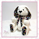 Regular Jointed Memory Bunny made with white fur and floral clothing, seated in a three-quarter front view.