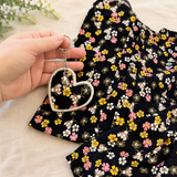 Hand holding a floral memory heart keyring beside the original loved one’s clothing used to create it.